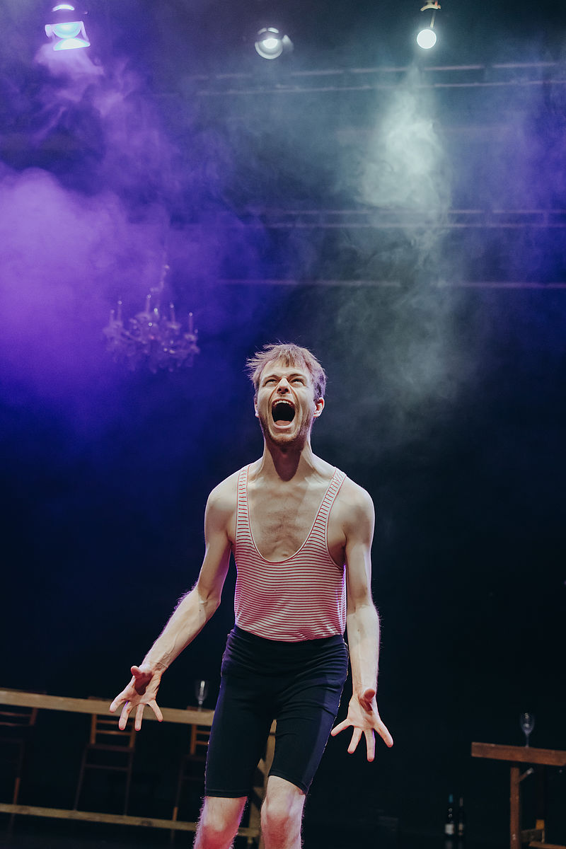 Ein Schüler steht schreiend und angespannten Muskeln auf einer Theaterbühne
