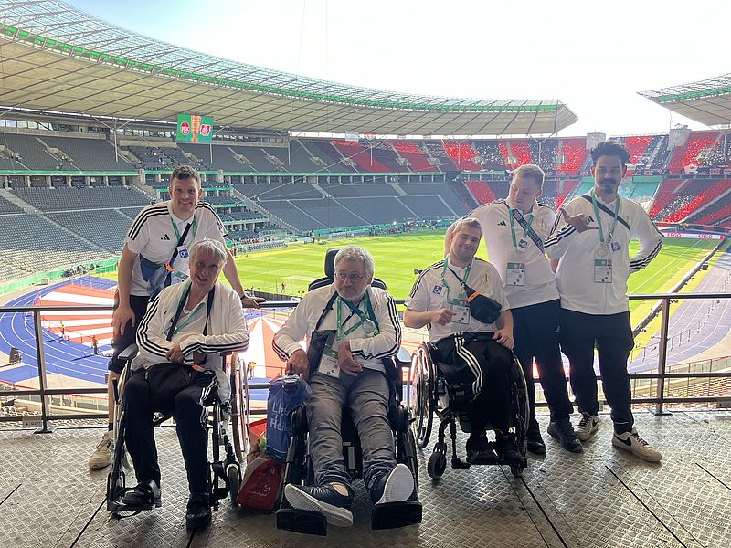 6 Personen - davon drei im Rollstuhl - im Olympiastadion Berlin. Sie tragen Volunteer-Kleidung des DFB.