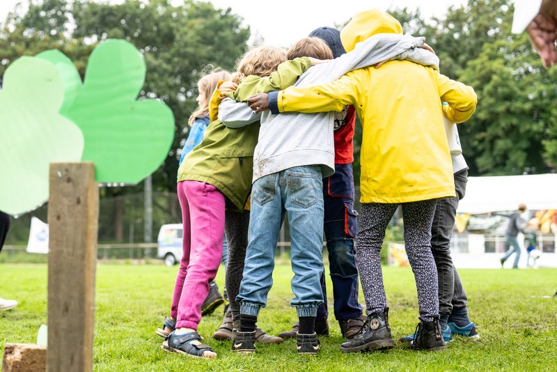 Mehrere Kinder stehen in einem Kreis zusammen und haben die Arme umeinander gelegt.
