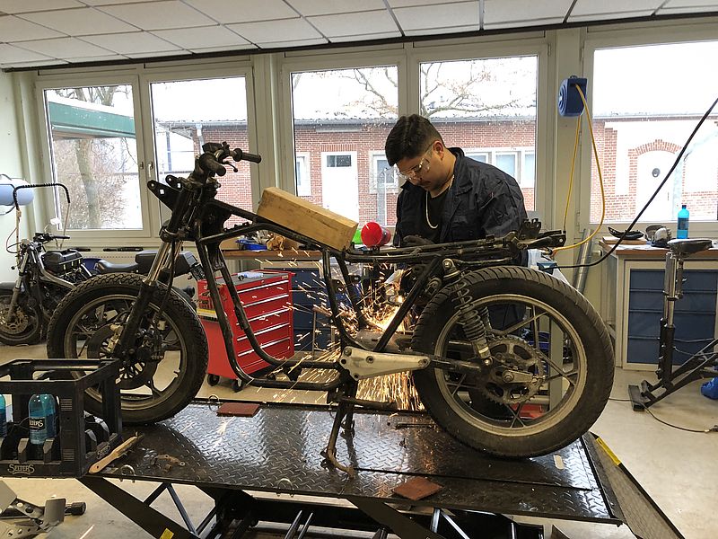 ein Jugendlicher arbeitet mit einer Flex an einem Motorrad
