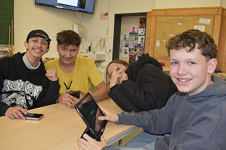 4 Jugendliche lachen in die Kamera. Ein Junge hat ein Tablet in der Hand