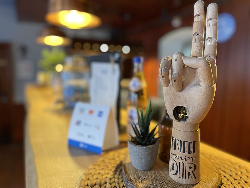 Eine Holzhand in Segenshaltung steht auf einer Theke