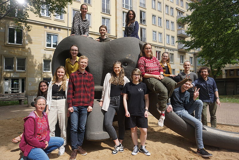 Ca. 15 Menschen sitzen auf und stehen vor einer Rutsche in einem Innenhof