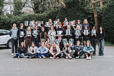 Berater:innen halten Schilder mit den Buchstaben der Refugee Law Clinic Bonn e.V. hoch