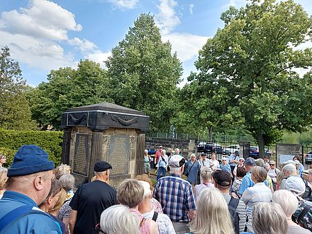 zahlreiche Menschen sind um ein Denkmal versammelt