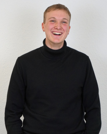 Mann mit Rollkragen Pulli der in die Kamera lacht