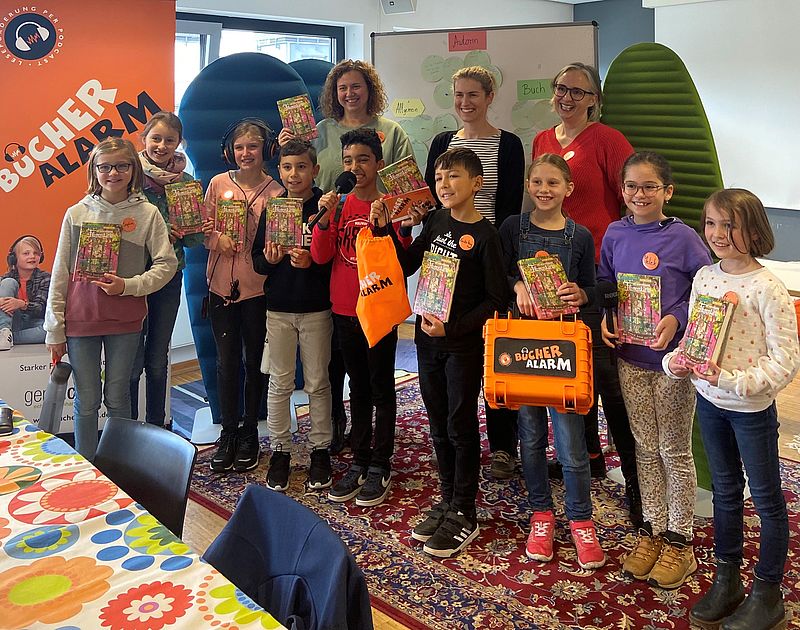 Kinder und Erwachsene stehen in einer Gruppe zusammen und halten Bücher in der Hand