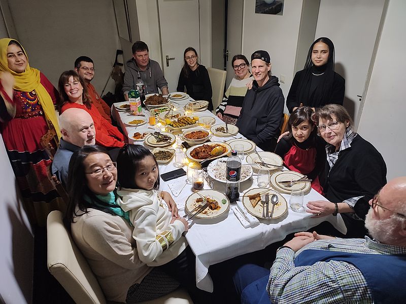 In vier Kanus sitzen jeweils vier erwachsene Personen unterschiedlicher Herkunft mit angelegten Schwimmwesten und winken mit ihren Stechpaddeln.