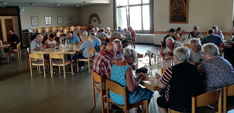 Menschen sitzen an Tischgruppen beim Mittagessen