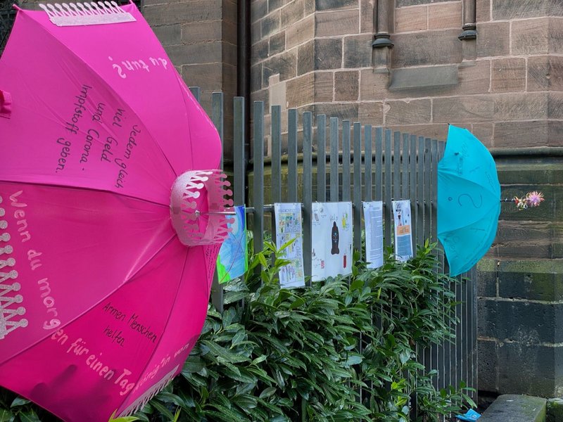 Schutzschirme und Bilder ausgestellt am Zaun der Johanneskirche