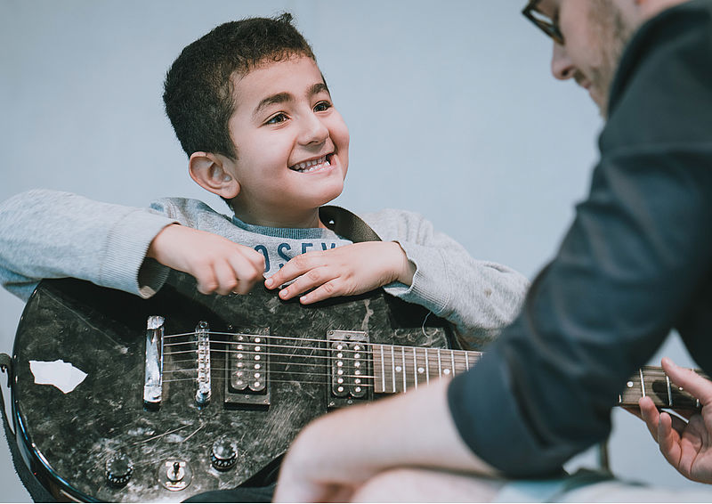 Ein Junge wird an der E-Gitarre angeleitet