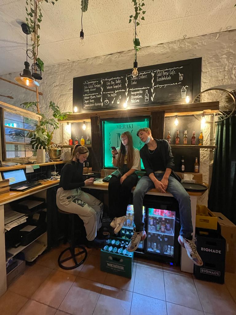 Drei Jugendliche sitzen auf der Theke eines Caféraumes und schauen auf ihr Telefon