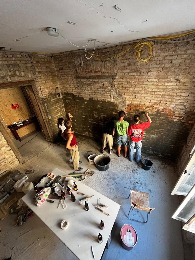 Menschen werden von oben fotografiert wie sie gemeinsam eine Wand verputzen